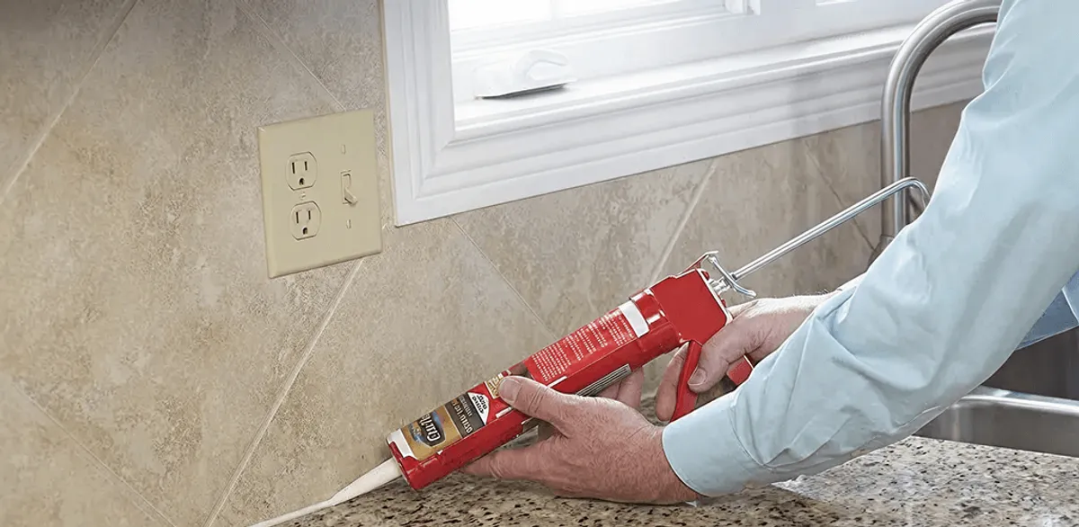 Handyman applying caulk along a kitchen backsplash and countertop seam in Worcester, MA