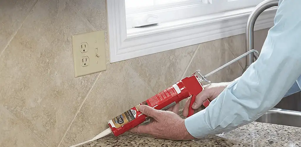 Handyman applying caulk along a kitchen backsplash and countertop seam in Worcester, MA