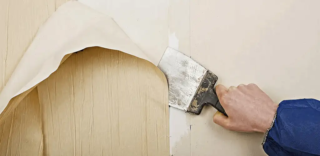 Handyman removing wallpaper with a scraper for wall preparation in Worcester, MA