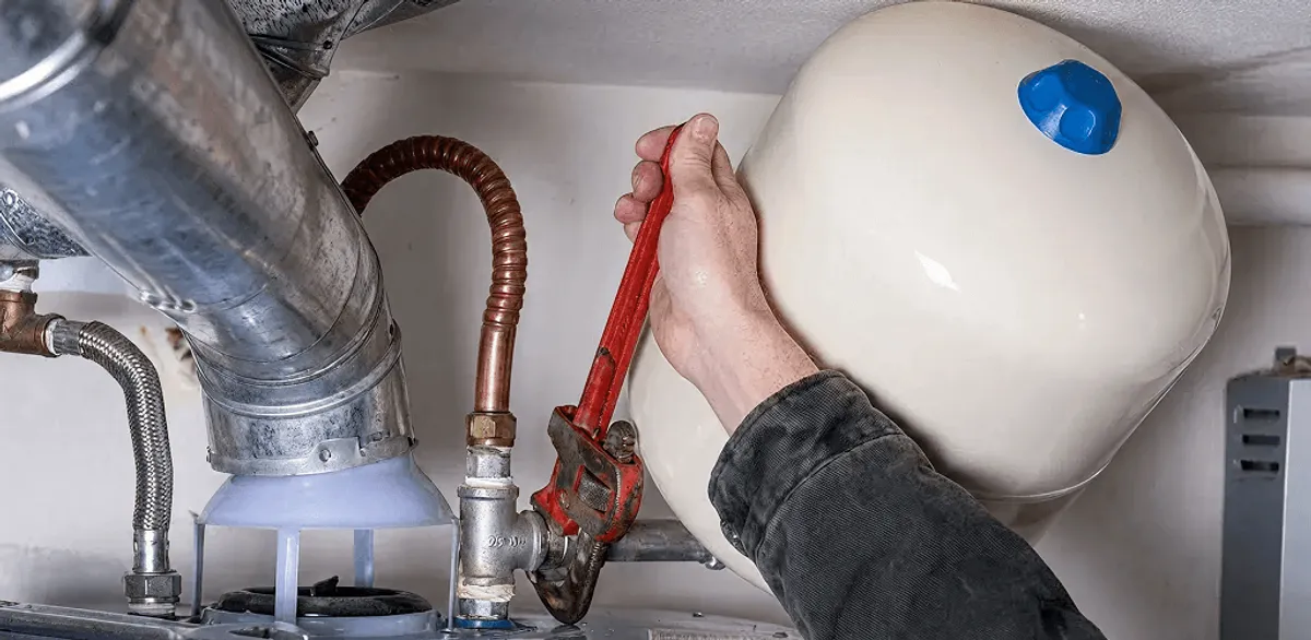 Water heater repair technician tightening plumbing connections near a tank unit in Worcester, MA